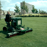 824153 Afbeelding van een medewerker van de gemeentelijke plantsoenendienst met een gemotoriseerde grasmaaier in het ...